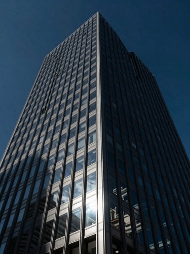 Low-angle dramatic architectural shot of a modern glass skyscraper reflecting a deep blue sky, sharp side-lighting, high contrast, 35mm lens