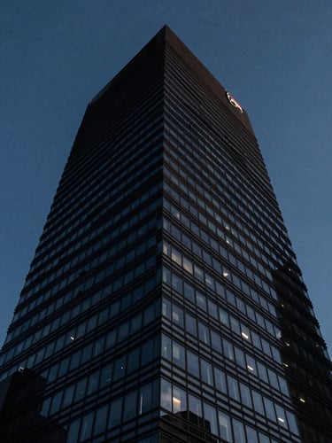 Low-angle architectural shot of a modern dark-glass skyscraper corner cutting into a deep blue dusk sky, sharp side-lighting, high contrast, 35mm lens