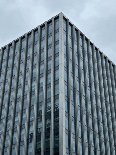 Architectural portrait crop of a modern corporate skyscraper corner, clean steel lines against an overcast gray sky, cool tones, 35mm