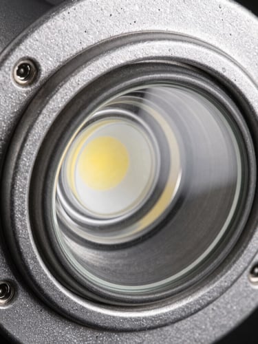 Macro close-up of an IP67-rated LED recessed floor light, focusing on the textured die-cast aluminium housing and tempered glass, hard directional studio light, steel tones, sharp focus.