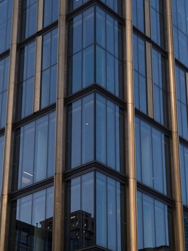 Close-up of modern financial district architectural glass facade, sharp angles, reflection of blue-hour sky, gold-tinted metallic accents, 35mm editorial corporate photography