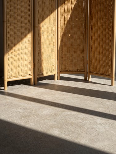 Architectural concrete patio in harsh afternoon sun, a rattan folding screen casting dramatic geometric shadows, warm sandy-beige tones, sharp focus, 35mm lens