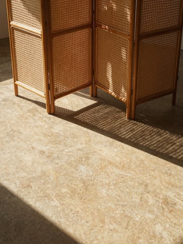 Wide-angle architectural editorial shot of a rattan folding room divider casting high-contrast geometric shadows on a warm sandy concrete floor, harsh direct sunlight, 35mm lens.