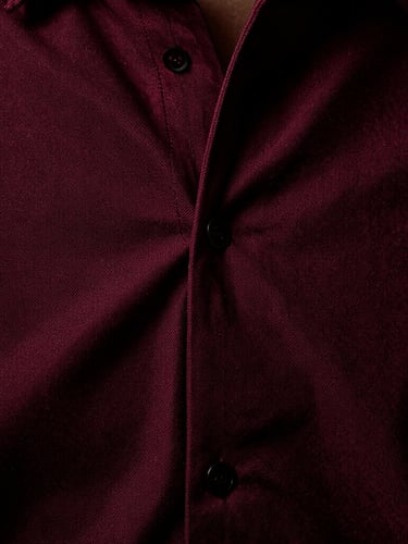Macro close-up of heavy oxblood-red shirting seams and zero-tension weave texture, high-contrast directional studio lighting, deep shadows, medium format film