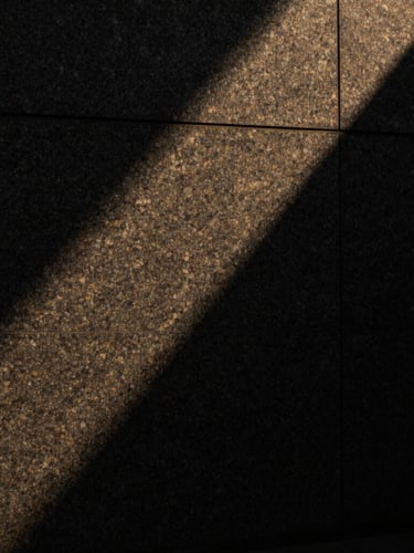 Abstract sharp shadows cast across a dark, textured granite wall, minimal architectural lines, low-key side lighting, premium quiet atmosphere