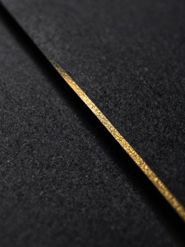 Macro close-up of heavy textured charcoal paper with a single, ultra-fine gold foil line along the edge, low-key dramatic side lighting, deep shadows