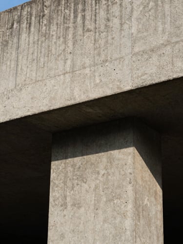High-contrast close-up portrait of raw, textured concrete structure in Accra, hard direct midday sunlight casting deep architectural shadows, brutalist form.