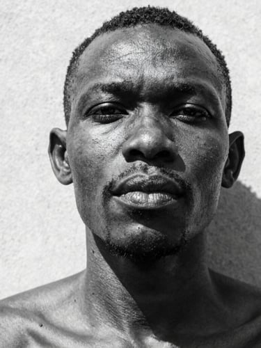 Extreme close-up portrait of a Ghanaian athlete in high-contrast black and white, direct harsh midday sunlight casting deep shadows on skin and concrete, raw texture, low angle.