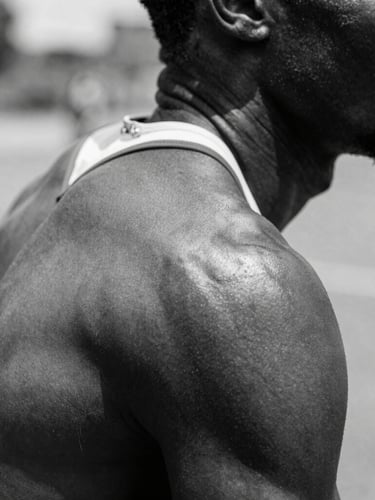 High-contrast black and white close-up of a Ghanaian athlete's shoulder in motion, hard direct sunlight casting deep shadows, raw skin texture.