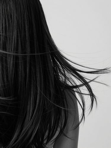 Close-up of rich, flowing dark hair texture with elegant movement, minimalist studio photography, soft diffused light, monochrome palette, sharp focus