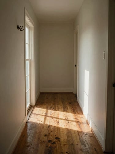 Wide interior hallway of an older home, morning light falling through a side window onto worn hardwood floors, a coat hook and doorframe to the left, soft warm shadows, quiet and still, no people