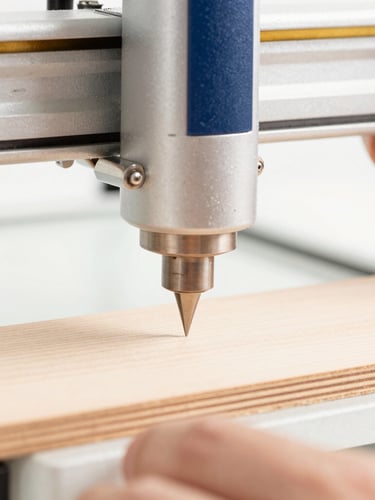Close-up of hands operating a precision laser engraver on a piece of wood, sharp textures, bright natural side-light, clean white backdrop, warm gold accents, 50mm