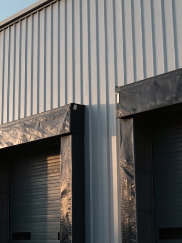 Abstract architectural close-up of a modern warehouse loading dock, corrugated steel panels in cool morning light, minimal geometric shadows.