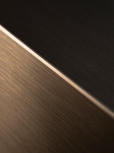 Extreme close-up of a brushed gunmetal sculpture catching dramatic low-key light, showing razor-sharp metallic edges and fine material grain, 35mm