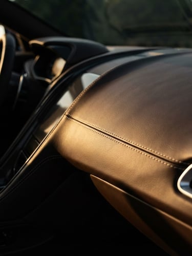 Extreme close-up of a luxury vehicle's leather interior, focusing on sleek dashboard lines and premium stitching, low-key dramatic lighting, wide-angle lens, high-contrast rich tones.