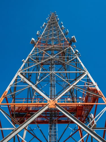 Low-angle heroic shot of a heavy steel telecom tower looking upward against a crisp desert sky, sharp industrial photography, high-contrast steel tones.