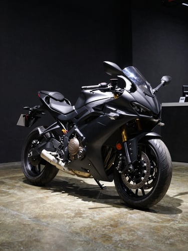 Wide showroom interior, a matte black sport motorcycle centered under a focused overhead studio strobe, hard shadow cast precisely on polished concrete floor — shot from a low 3/4 front angle, the bike occupying the right two-thirds of the frame, deep black background to the left