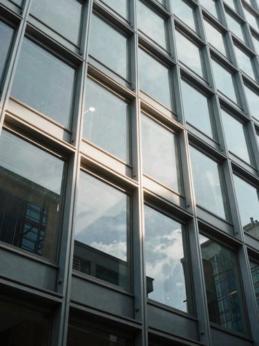 Low-angle architectural photograph of a structural glass facade, crisp daylight casting sharp geometric shadows on aluminum profiles.