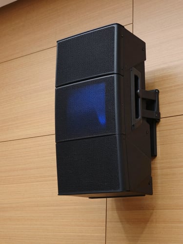 Close-up architectural shot of a sleek line-array speaker column flush-mounted to a minimalist wood-paneled auditorium wall, natural lighting, sharp focus, 35mm