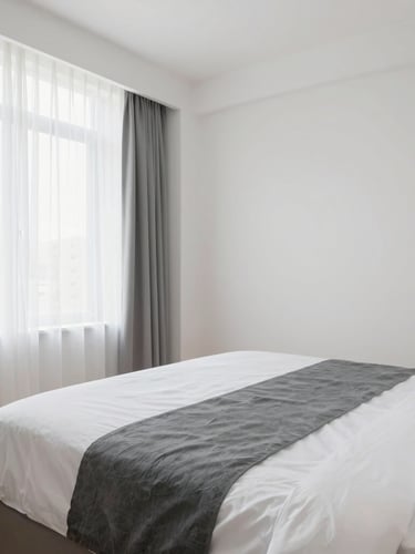 Wide spacious architectural crop of an empty, perfectly styled boutique hotel bed with crisp white sheets and slate grey runners, soft daylight.