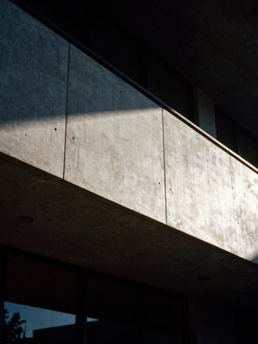 Dramatic low-key architectural detail of a modern concrete and steel facade in Phoenix, sharp shadow lines from late afternoon sun, high contrast, dark moody editorial photography, 35mm film