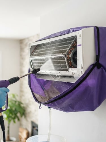 Close-up of a mini-split indoor head being pressure-washed with a protective bib inside a Sackville home, bright natural daylight, clean purple and white tones