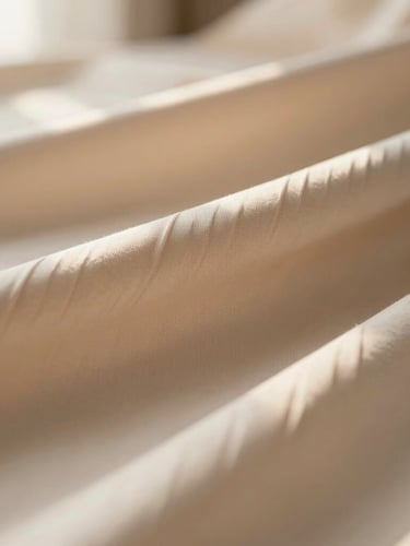 Close-up macro shot of premium beige and cream pleated fabrics, soft morning sunlight, shallow depth of field, warm minimalist aesthetic