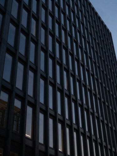 Imposing modern corporate building facade at dusk, sharp architectural lines, dramatic low-key lighting, reflecting deep navy and charcoal tones, viewed from a low angle, cinematic, 35mm.