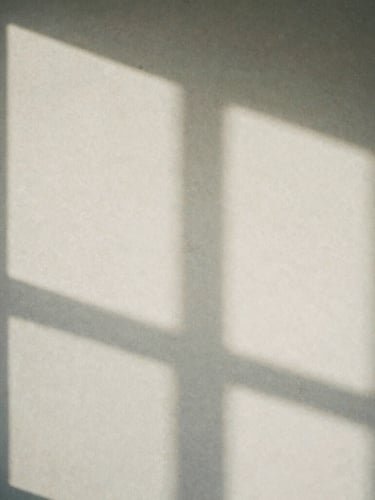 Minimalist close-up of soft shadows cast by a window frame onto a textured stone wall, soft diffused daylight, quiet contemplative atmosphere, matte paper feel