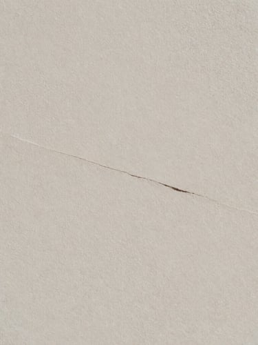 Minimalist editorial photography, soft diffused north-facing daylight. An extreme close-up of natural stone texture with a subtle, elegant crack running diagonally, casting quiet shadows. Matte paper texture, muted mineral tones, 35mm film.