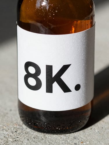 Extreme close-up of an amber glass bottle on a rough concrete surface, harsh directional studio lighting casting deep shadows, showing a clean white technical label with bold black typography.
