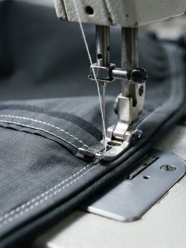 Close-up macro shot of a sewing machine needle precisely stitching a high-performance technical fabric, crisp bright industrial lighting, high contrast, 35mm