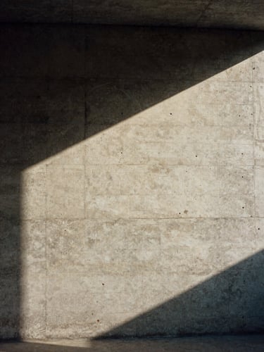 Cinematic film photography of a concrete modernist studio wall with a single ray of sharp sunlight cutting across the raw texture, desaturated earth tones, 35mm grain