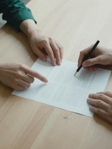Overhead view of two professionals analyzing a printed document on a light oak table, soft natural shadows, minimalist aesthetic, focus on hands and paper.