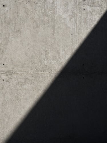 Extreme close-up of raw concrete corner with dramatic diagonal shadow, stark high-contrast natural daylight.