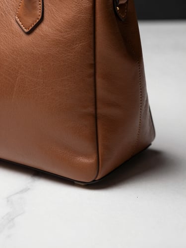 Close-up of a leather handbag on a white marble surface, directional studio strobe light creating a clean shadow beneath the bag's edge, product detail sharp