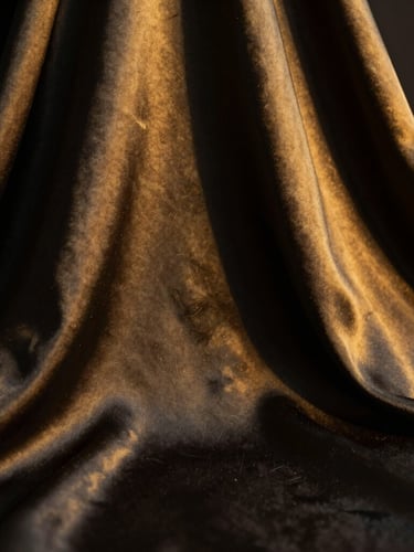 Close-up of premium satin silk fabric draping elegantly, soft golden light catching the weave texture, deep shadows, luxurious minimalist fashion aesthetic, 35mm