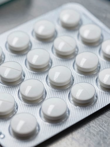 Close-up macro shot of white scored tablets arranged in a blister pack on a stainless steel manufacturing surface, clinical overhead lighting, sharp focus on pill embossing detail, no shadows, documentary industrial framing