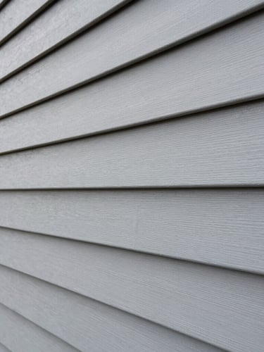 Close-up macro shot of crisp gray vinyl siding panels perfectly aligned on a residential exterior, sharp construction photography, bright daylight.