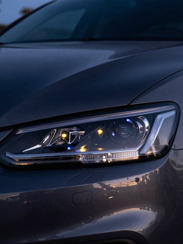 Close-up macro shot of a clean modern car headlight reflecting downtown Tucson streetlights at twilight, deep charcoal tones