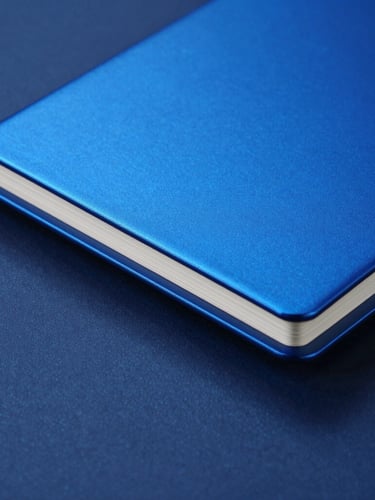 Macro studio shot of a sleek, custom-branded anodized aluminum notebook with electric blue metallic edge gilding, crisp lighting, deep blue shadows, 50mm
