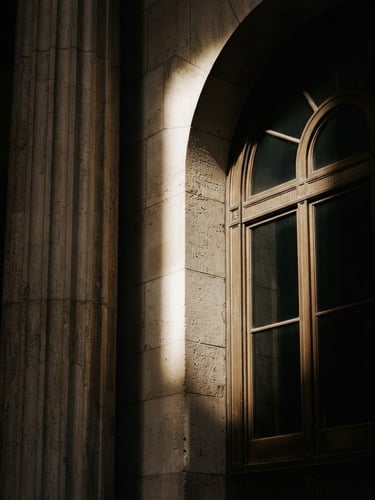 A minimalist architectural detail of a historic financial building in New York, sharp directional window light, deep shadows, desaturated warm tones, high-contrast 35mm.
