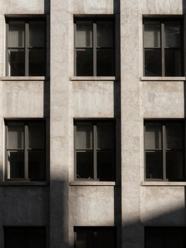 Stark minimalist architectural detail of a historic financial building facade, sharp directional window light casting deep geometric shadows, desaturated warm tones, high-contrast 35mm composition with generous negative space