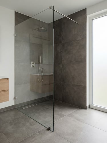 Wide shot of a modern, minimalist zero-threshold shower with large format charcoal tiles, natural light from a frosted window, pristine glass partition, and a sleek linear drain. Clean architectural photography, soft natural daylight, desaturated charcoal and white tones, sharp focus.