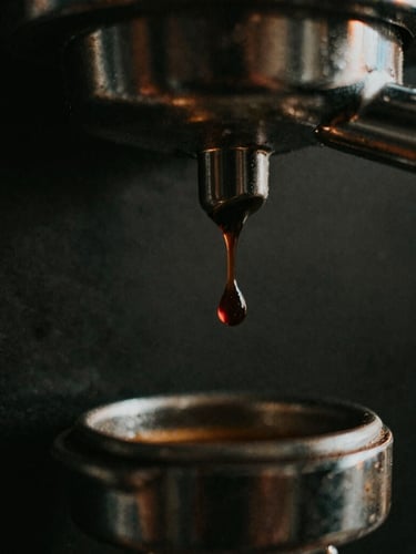 Macro close-up of a single dark espresso drop falling from a bottomless portafilter, golden-hour side lighting, moody dark background, 35mm film style.