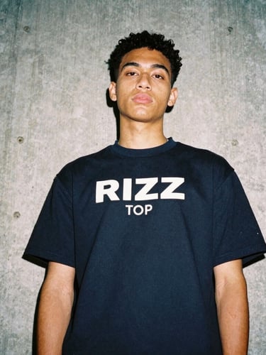 Candid low-angle shot of a Gen Z model wearing a Rizz Top in an urban concrete setting, direct flash photography, 35mm film look.