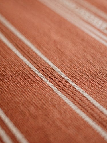 Macro close-up of warm terracotta hand-woven Indonesian tenun textile, rich organic thread textures, soft natural side-light, shallow depth of field, 35mm film