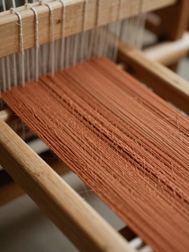 Macro close-up of raw terracotta-colored woven threads on a traditional wooden loom, soft directional side-light, rich organic textures