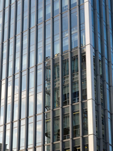Architectural close-up of a modern European financial district building with clean glass facade reflecting bright morning sunlight.