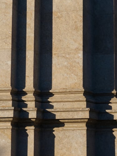 Abstract architectural detail of a structural stone column, crisp natural daylight with sharp shadows, deep navy and muted gold tones, 35mm